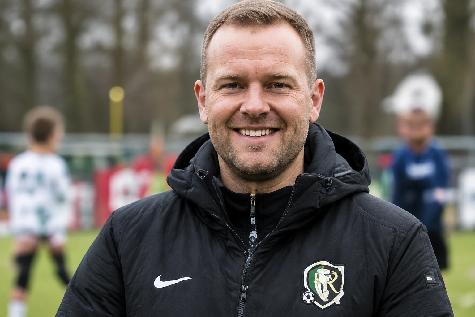 Vrijwilliger Thijs lachend in zijn clubjack op het sportpark